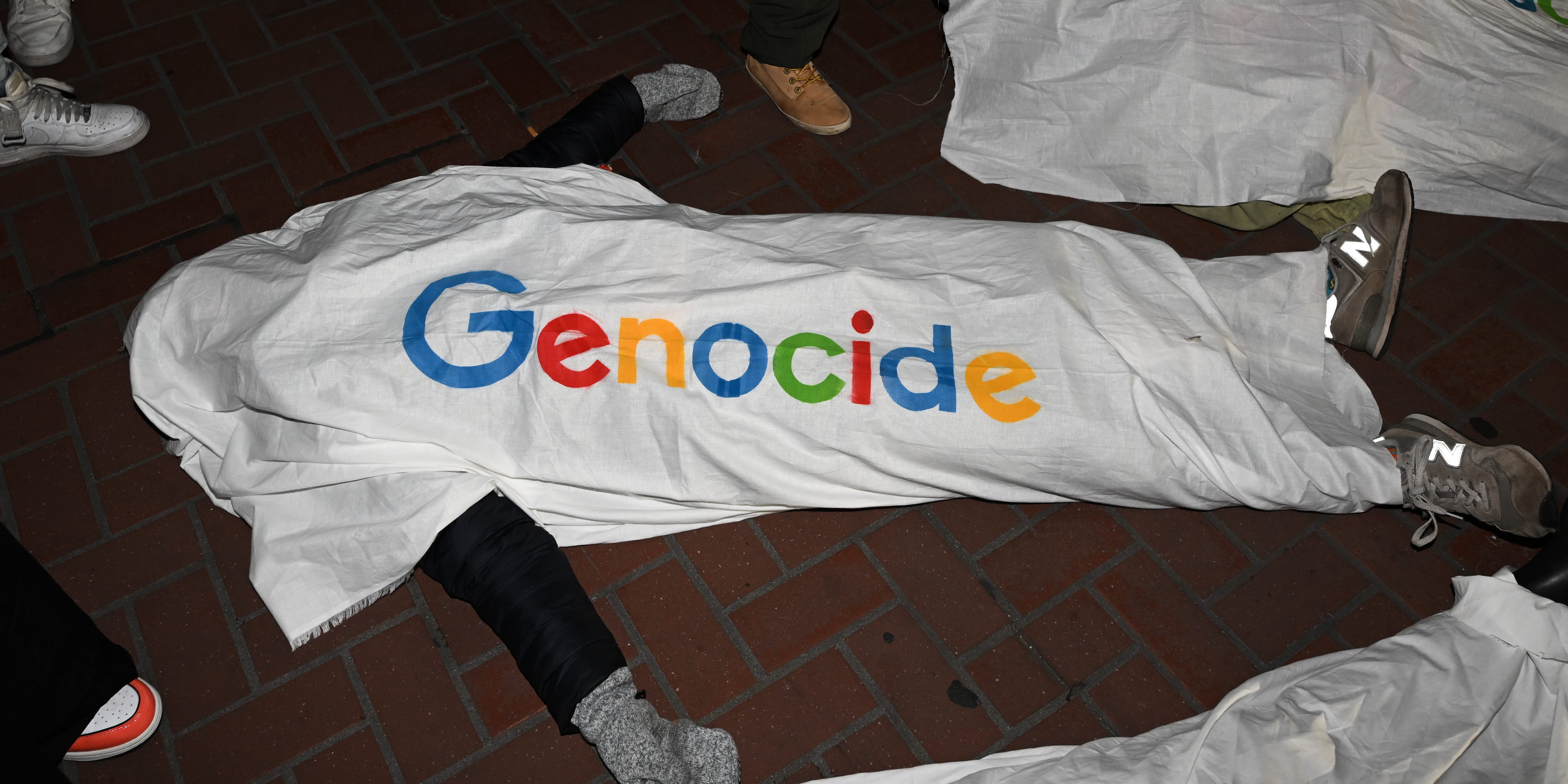 SAN FRANCISCO, CALIFORNIA - DECEMBER 14: About a dozen demonstrators lay on the ground draped in white sheets with a mock version of the Google logo spelling out the word 'genocide', as hundreds of protestors including Google workers are gathered in front of Google's San Francisco offices and shut down traffic at One Market Street block on Thursday evening, demanding an end to its work with the Israeli government, and to protest Israeli attacks on Gaza, in San Francisco, California, United States on December 14, 2023. (Photo by Tayfun Coskun/Anadolu via Getty Images)