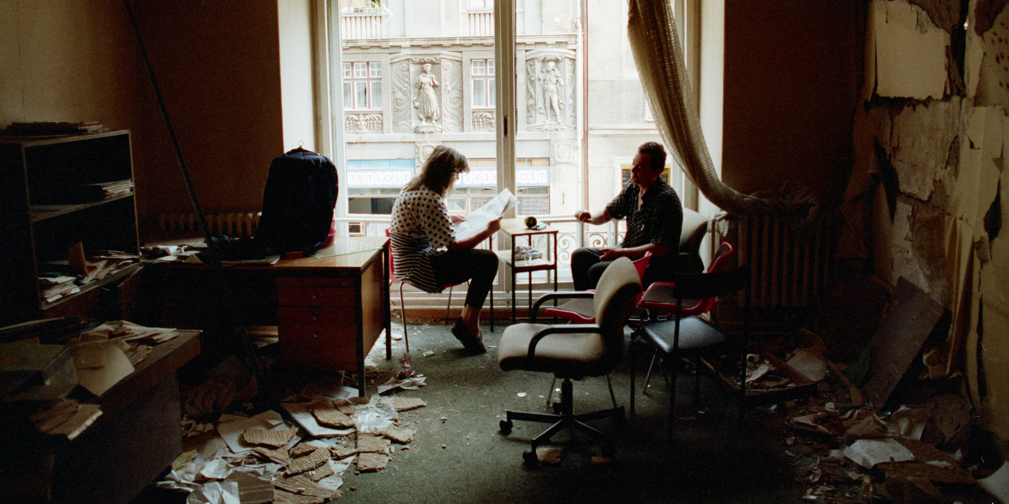 A Bosnian couple reads the newspaper in their bombed-out apartment along Marshal Tito Avenue in Sarajevo.   (Photo by David Turnley/Corbis/VCG via Getty Images)